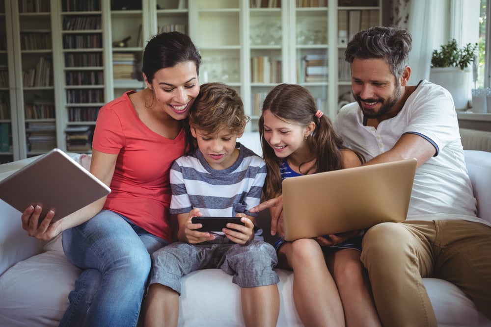 Happy family sitting on sofa and using laptop, mobile phone and digital tablet at home